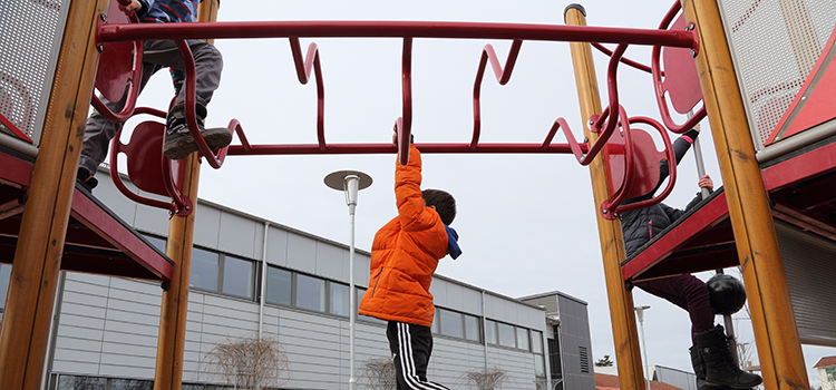 Ett barn i orange jacka hänger i en klätterställning utanför Trekantenskolan