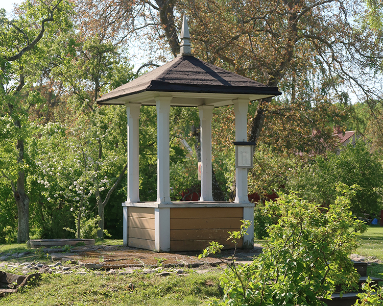 Brunnen med sin överbyggnad. Den har en gulbrun nederdel, vita pelare och ett mörkt tak.