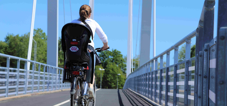 Kvinna med cykelbarnstol på pakethållaren cyklar över en cykelbro.
