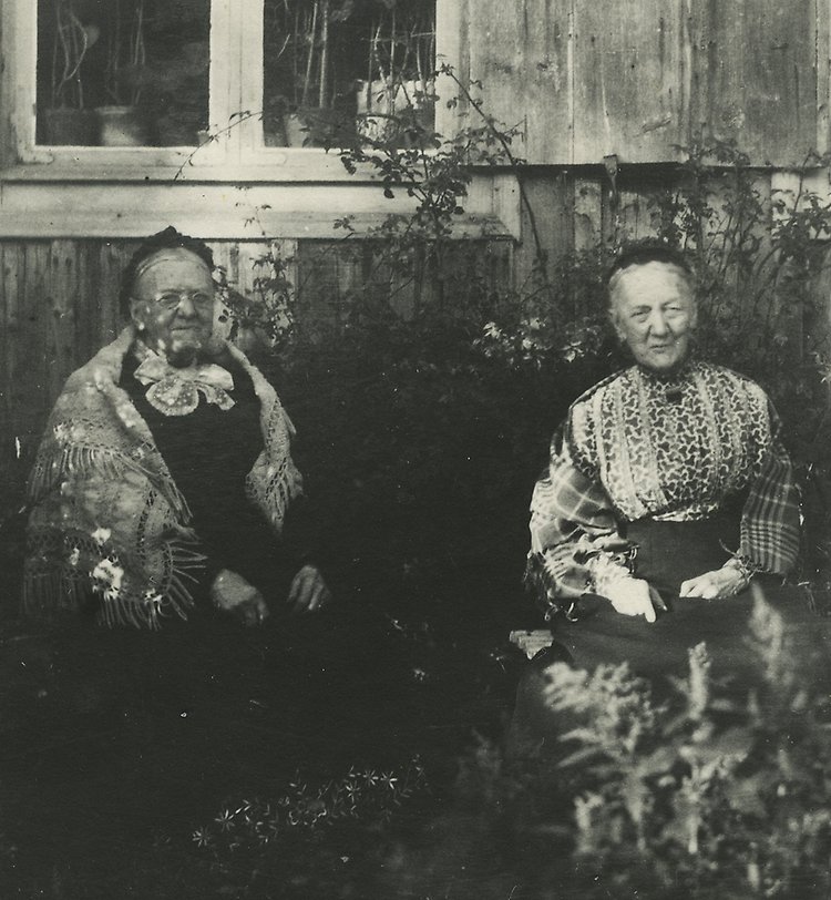 Svartvitt fotografi på två äldre kvinnor i en trädgård.