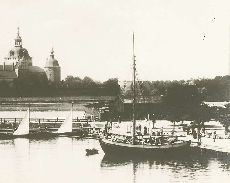 Fotografi från tidigt 1900-tal av Slottsfjärden. I förgrunden syns en båt och i bakgrunden Kalmar slott. Bakom båten finns träbyggnader som inte står kvar idag. 